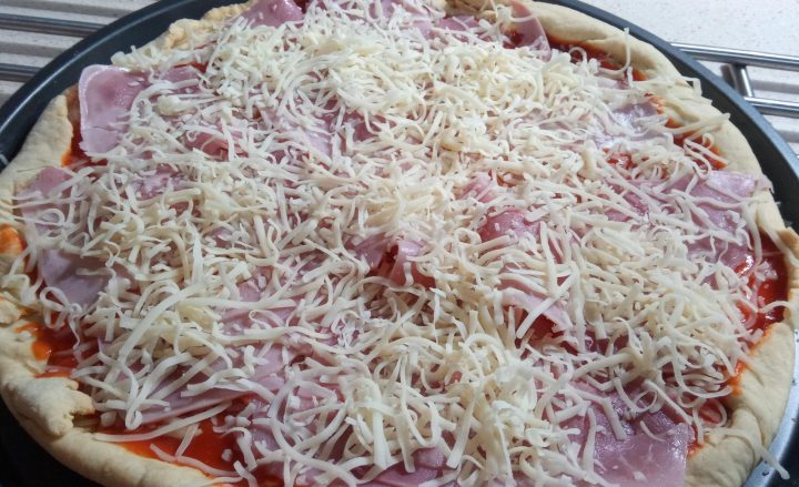 Echar queso y jamón york en la masa de la pizza.